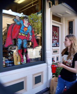 Senior Ingrid Reed paints superman on the window of downtown store Oh, Olive!