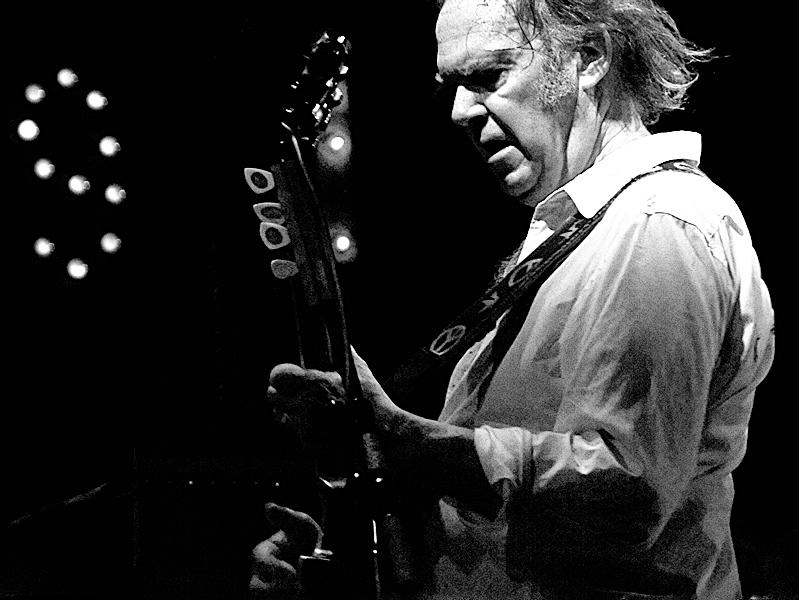 Neil Young rocks out with his guitar on stage. 