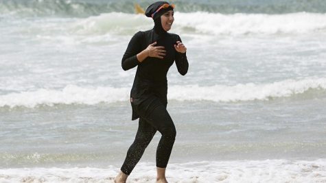 A woman jogs along the beach, while wearing a burkini.
