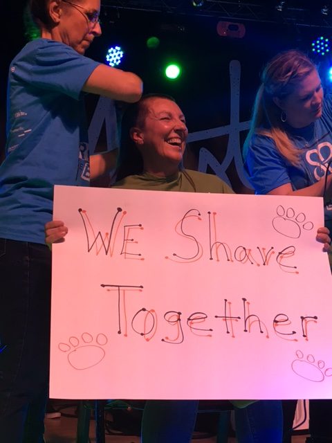 LHS special education teacher Kim Jansen brandishes her sign as one of the St. Baldrick’s volunteers begins shaving her head. 