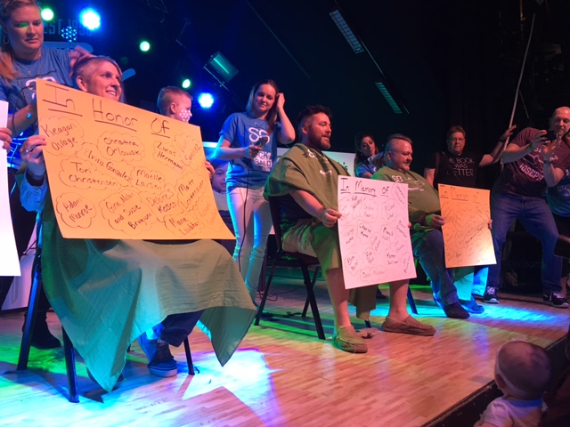 From left to right, LHS teachers Amy Holtsford, Brady Sullivan, and Mike Mansell hold up their “In Honor Of” and “In Memory Of” signs, which help to explain why these teachers chose to have their heads shaved.
