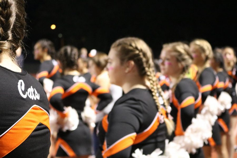 Varsity cheerleaders stand on the sidelines during the national anthem at the game on Friday, Oct. 20. All of the cheerleaders had a pink ribbons at the ends of their braids in support of Breast Cancer Awareness. 