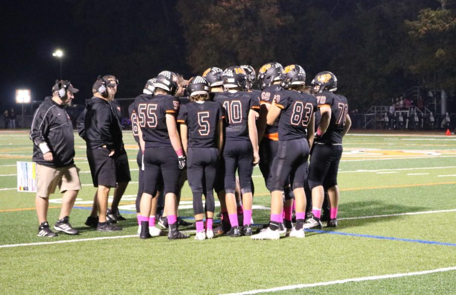 The football team huddles during a timeout to discuss team plays in their 43-20 win. They all wore pink socks in support of Breast Cancer Awareness.