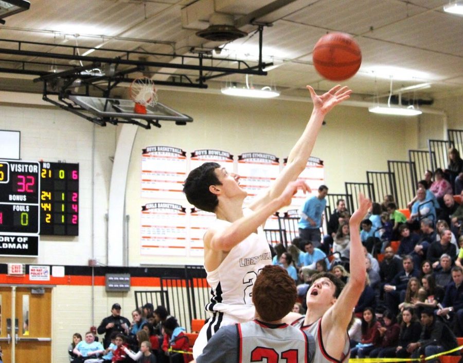 Battling for an offensive rebound, 6’8’’ senior forward Drew Peterson towers over two Mundelein players as he reaches for the ball.