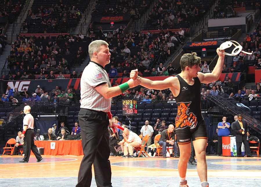 Pucino’s victory in the Class 3A 132-pound weight group third-place match is announced by the referee, as he raises Pucino’s arm. Pucino waves to his teammates who supported him during the tournament, with his head gear in hand.