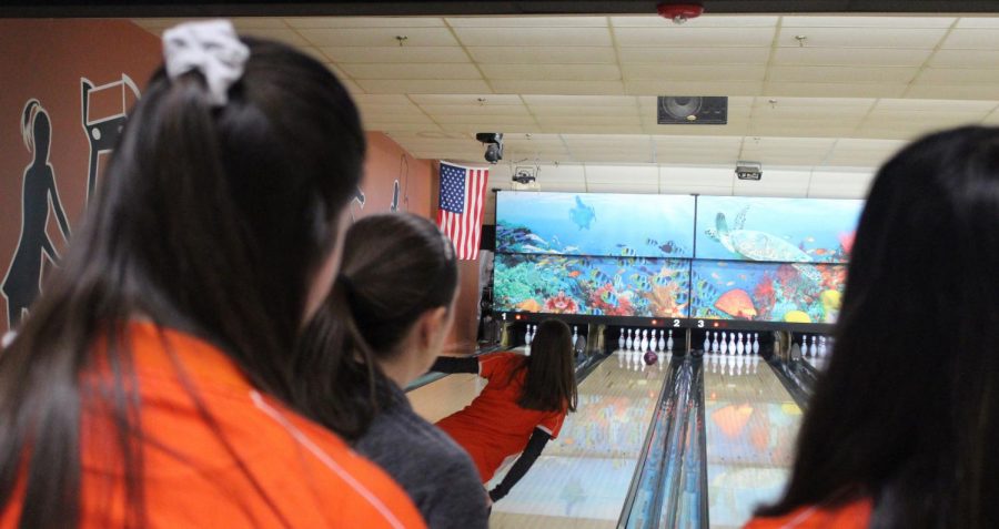As junior Kristine Kropp bowls, her teammates and coach observe closely.