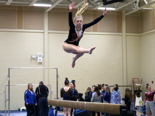 Skie, competing on the balance beam, jumps and folds at the hips while keeping one leg straight and the other leg bent. This is called the wolf jump.