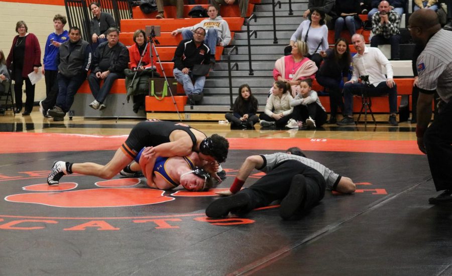 One of the referees gets close to the ground in order to verify if one of the Libertyville wrestlers gets a successful pin on the opponent.