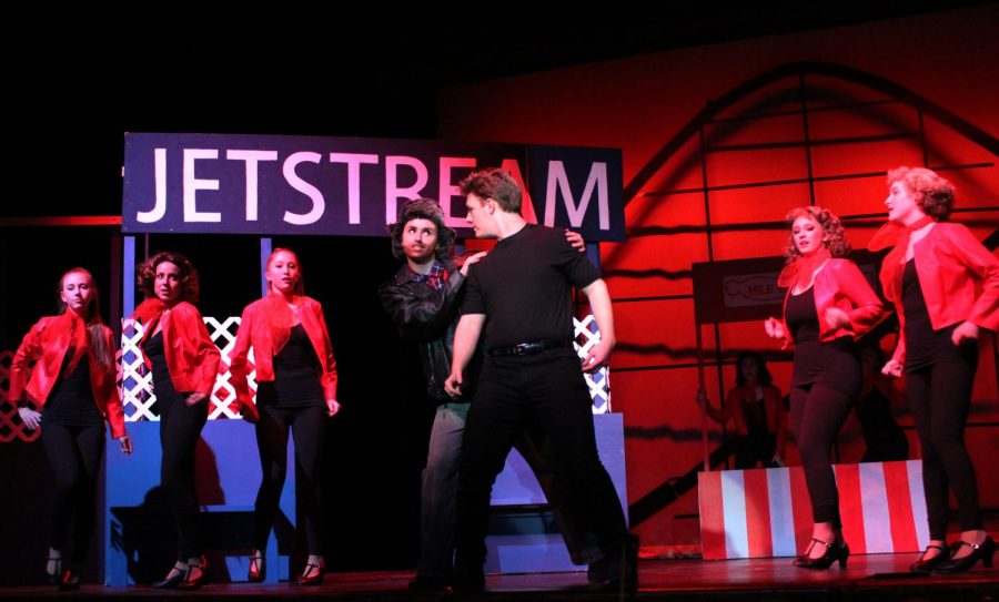 The musical is set in a small Midwest town in the summer of 1955, shown through the leather jackets and neck scarves worn by the ensemble. Erdmann and Sterner perform A Little Less Conversation in this scene.
