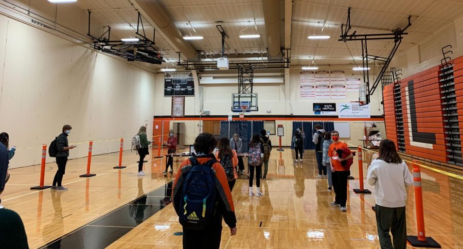 Students and staff line up, socially distanced in the Main Gym testing site, to scan their Navica app with Passport Health staff before conducting their tests.