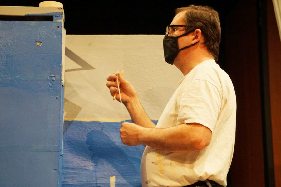 The crew creates the brick wall visual by placing masking tape over a base coat and then painting over it with the blue paint. Kevin Holly, the technical theater coordinator, helps with this process.