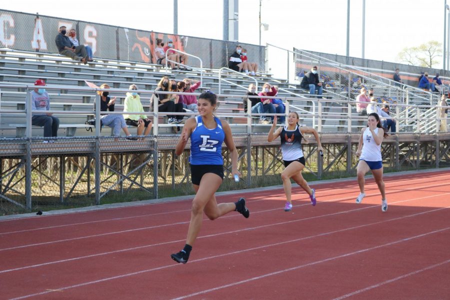 A Lake Zurich runner takes the lead in stride as she finishes her leg of the 4 x 200 relay race. LHS runner Dakota Lyons runs behind in a close second.