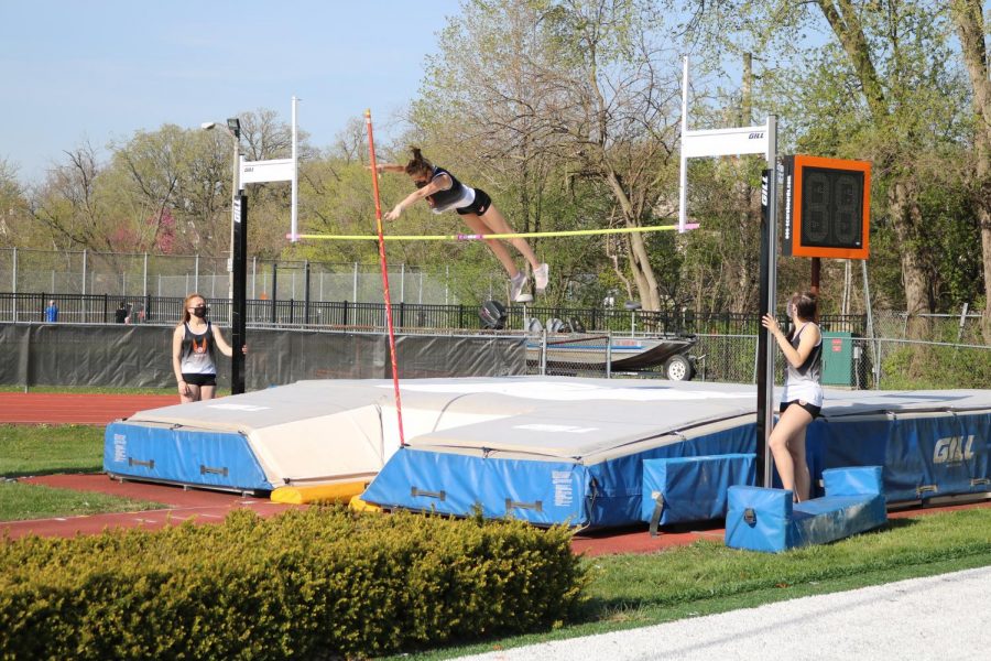 Rachel Birch cleanly clears the bar in the pole vault with her teammates watching her form from the sides.