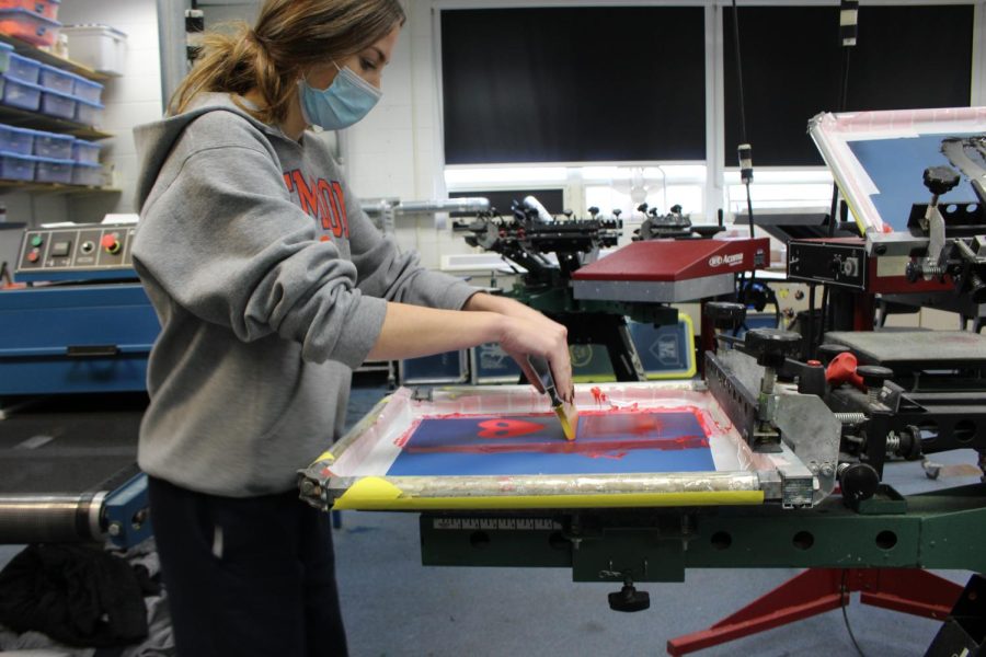 In Graphics class, students can create many projects, including screen printing . This involves creating a design on Adobe Illustrator, printing out their design on a vellum paper and exposing the design onto a screen to cure the emulsion. This student is pulling the ink over their design. 