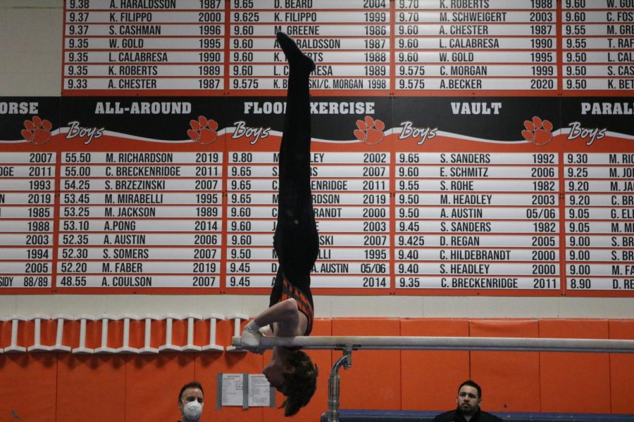 JV gymnast George Hanbury continues his parallel bar routine with a shoulder stand. His highest score of the night came during his vault routine in which he scored a 7.200 out of 10 points.