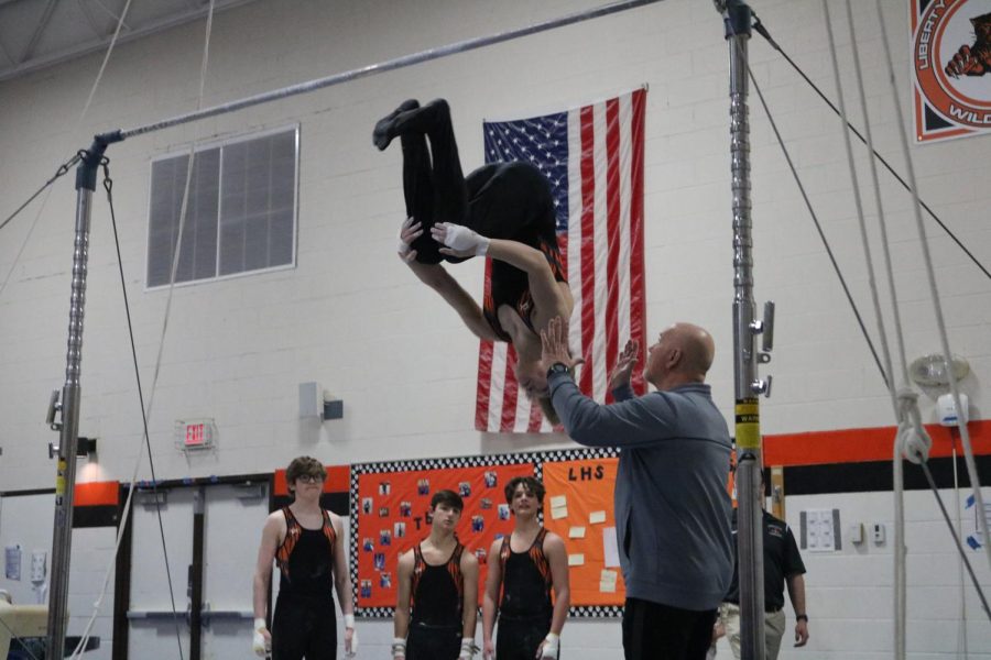 JV gymnast Max Butler finishes off his high bar routine with a fly away. His highest score of the night was on his floor routine which earned him 7.800 points out of 10.