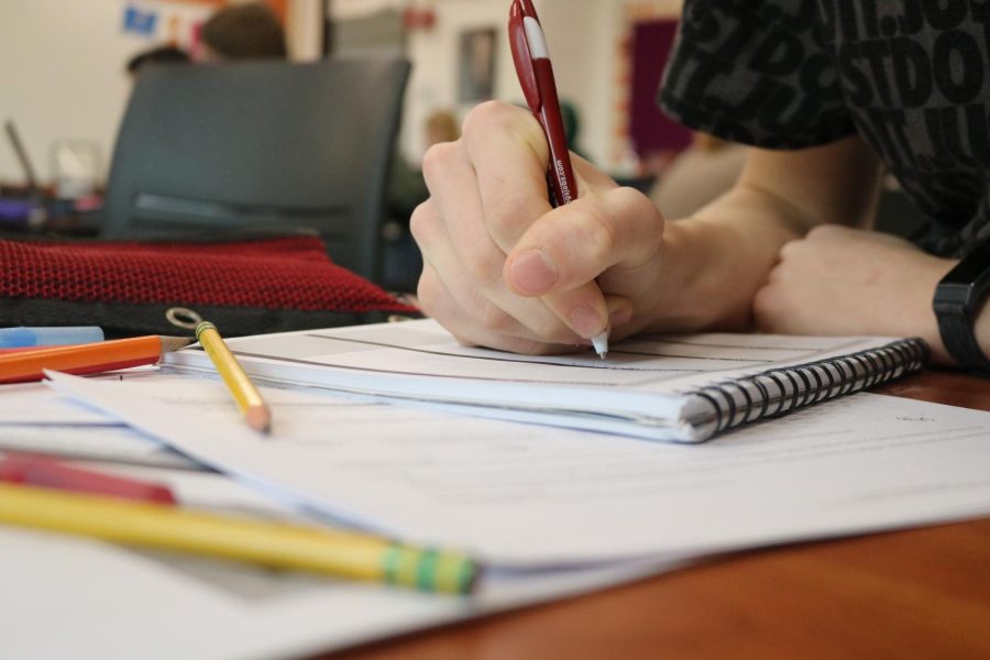 A student takes notes with pen and paper. Studies show that writing by hand strengthens conceptual understanding and awareness.