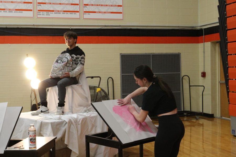 Art student sketches a randomly chosen observer of the show on the spot for another live exhibit presented. It gives the opportunity for students to “model” with a prop of their choice in order for them to experience the work the artists have put in.