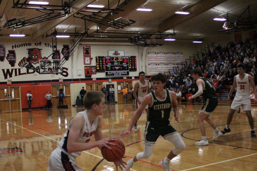 Senior Will Buchert (5) handles the ball just outside the 3-point line, facing pressure from a Stevenson opponent. Despite the pressure of Senior Night, the team ultimately pulled through to win the night by a point.