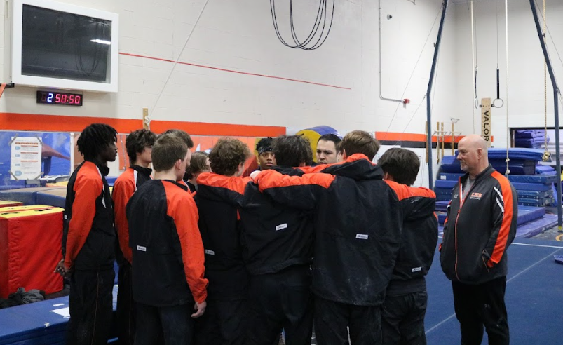 The boys gymnastics team, led by Coach Josh Cimo, convenes after the meet for a pep talk.