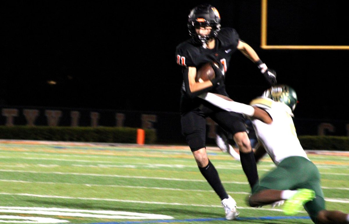 Junior Stevan Gavric (11) clutches the ball tightly as he faces pressure from a Stevenson opponent. Gavric, a wide receiver, had two touchdowns for the Wildcats over the course of the night.