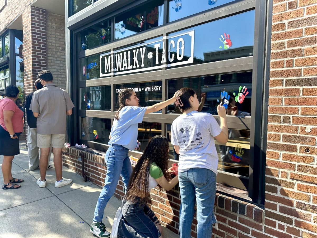 Some members of the Latin American Student Association (LASO) add hand prints with different Latin American countries and designs to Milwalky Taco’s dining entrance window.
