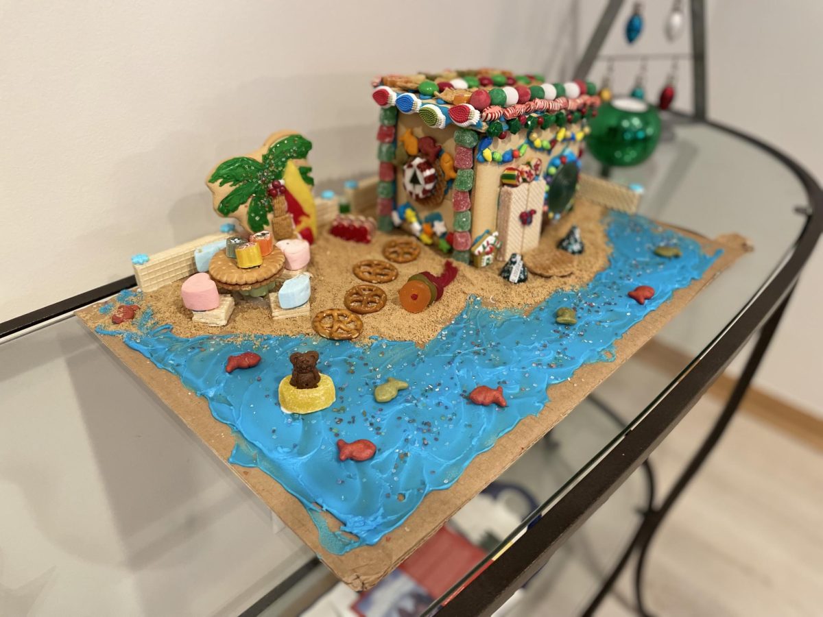 One notable gingerbread house that we made was a beach gingerbread house. The roof was decorated with candies like M&MS, Golden Grahams, sprinkles and peppermints. Unlike the traditional coconut snow that we use to finish off our gingerbread houses, crushed Graham crackers were used as sand and blue icing was used as water to help turn the gingerbread house into a beach house. In addition, a palm tree cookie was added for the palm tree and pretzels created a path to the beach house. 