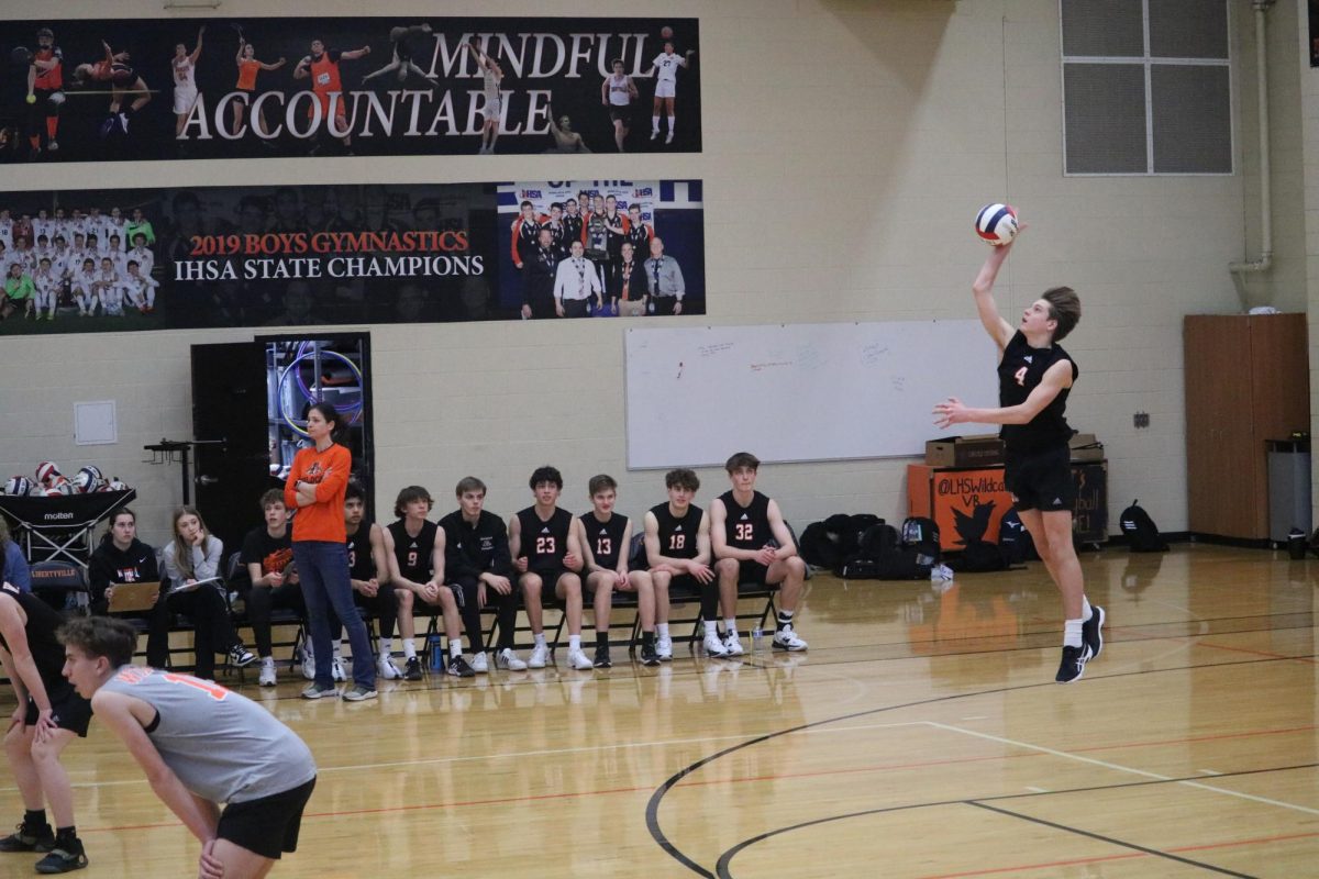 Junior defensive specialist and outside hitter Justin Howell (4) serves against the Titans in the first set. Justin had two digs across both sets in the game against Glenbrook South.