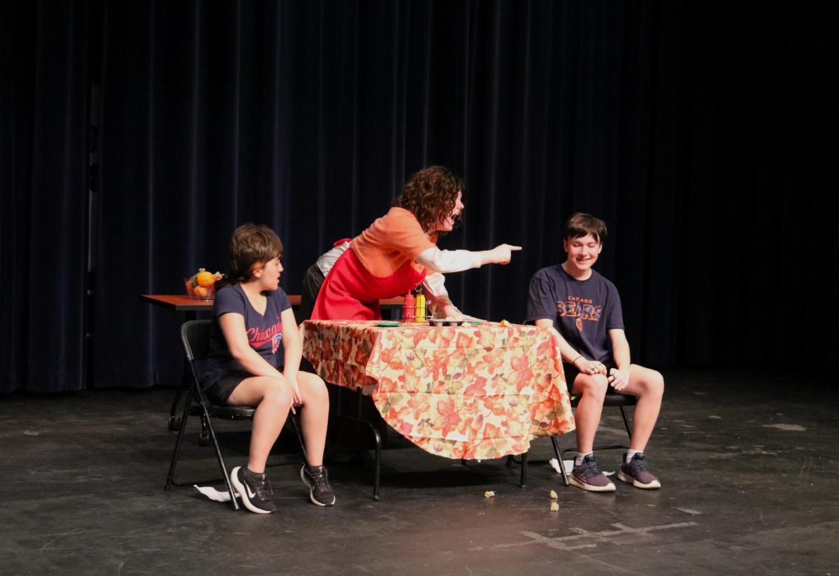 Sophomore Jack Boller, playing as the mother in an instant food commercial, points a finger at sophomore Lexi Likosar. Likosar, one of two sons, attempts to play along with the comedic attempts from the mother to follow instruction from the commercial director, junior Eva Thomas.