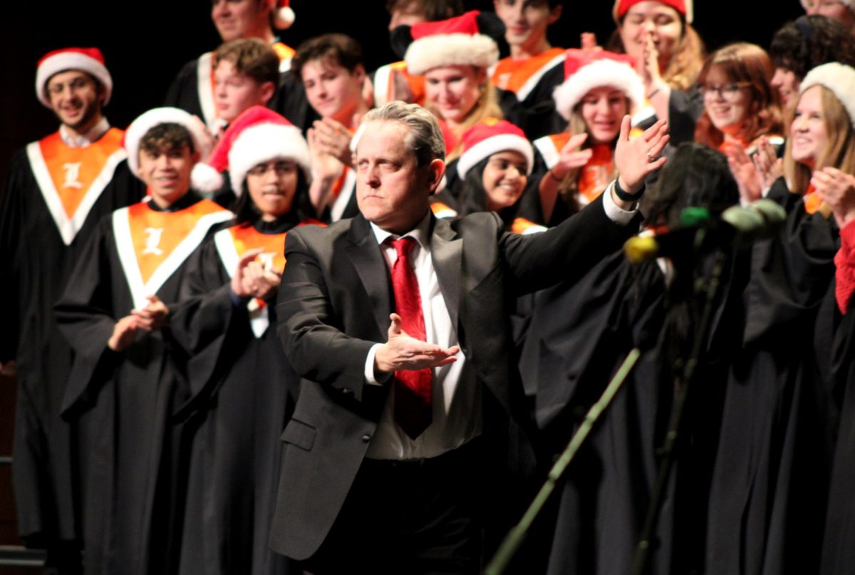 Dr. Jeff Brown, Choir Director, signals for the audience to give a round of applause to seniors Thomas Texiera, Zoe Mueller and sophomore Vince Lombardo for their respective performances on bass, guitar and drums. The band only came out to perform for "Run Run Rudolph," an audience favorite.